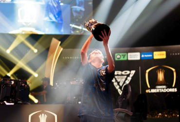 Troféu da CONMEBOL eLibertadores levantado por atleta em cima de um palco durante o evento de EA SPORTS FC 26.