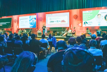 Fachada iluminada do pavilhão da gamescom latam 2026 no Distrito Anhembi, com banners de grandes marcas de jogos e público circulando.