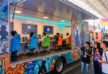 Caminhão tecnológico adaptado como hub móvel de games, estacionado em uma praça pública de São Paulo com jovens interessados ao redor.